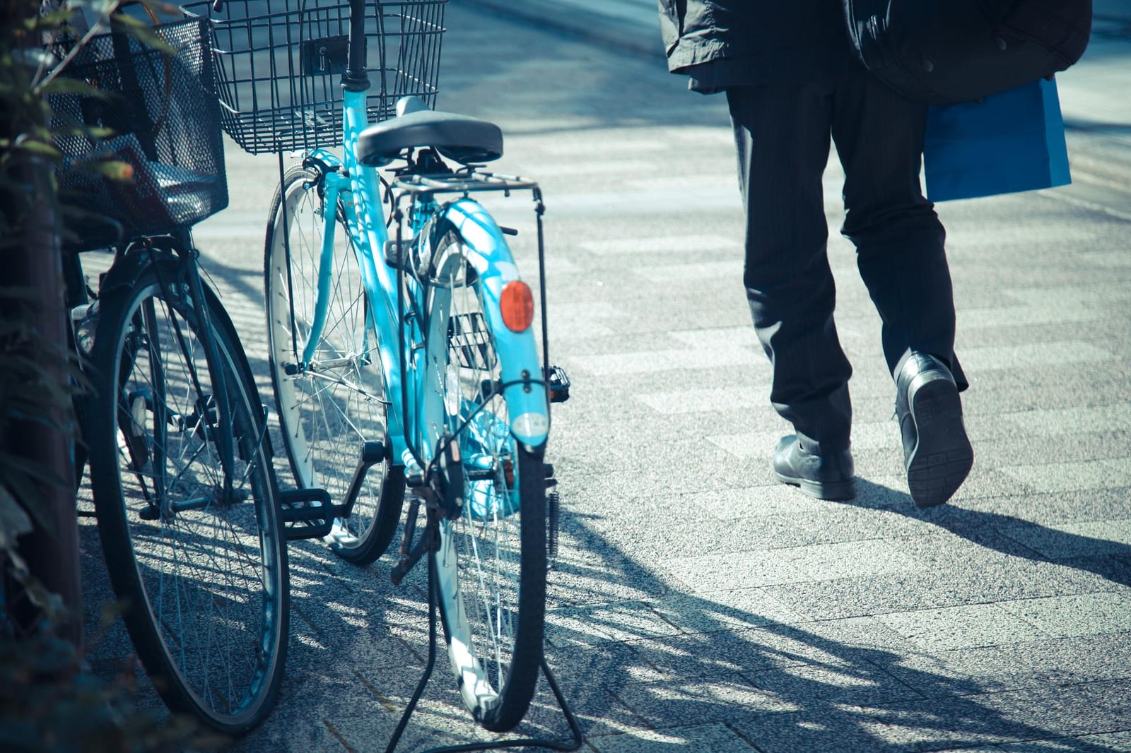 歩道に並ぶ自転車と、買い物袋を提げて通り過ぎる人の様子